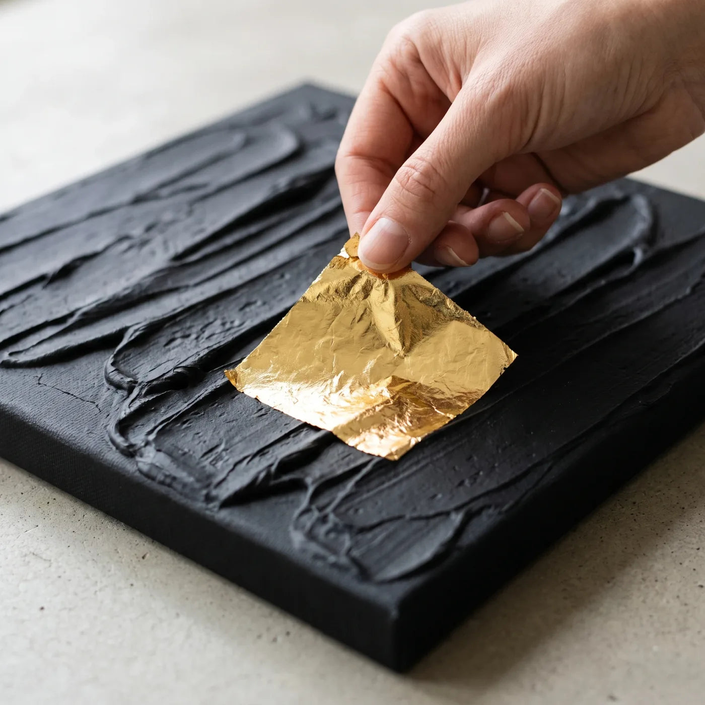 Auflegen eines Blattgoldbogens auf das schwarze Strukturrelief